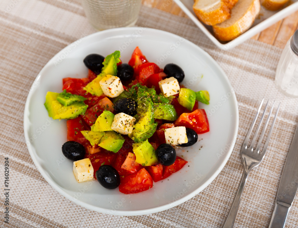 Just cooked avocado salad with chopped tomatoes, cheese feta served on plate with black olives.