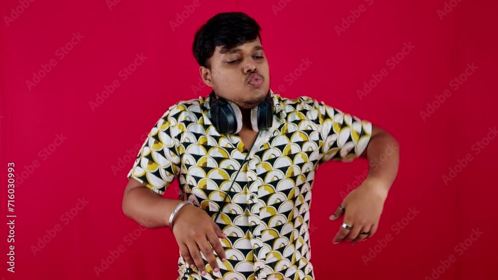 Man in patterned shirt with headphones around neck dancing against a red background Man in patterned shirt with headphones around neck dancing against a red background