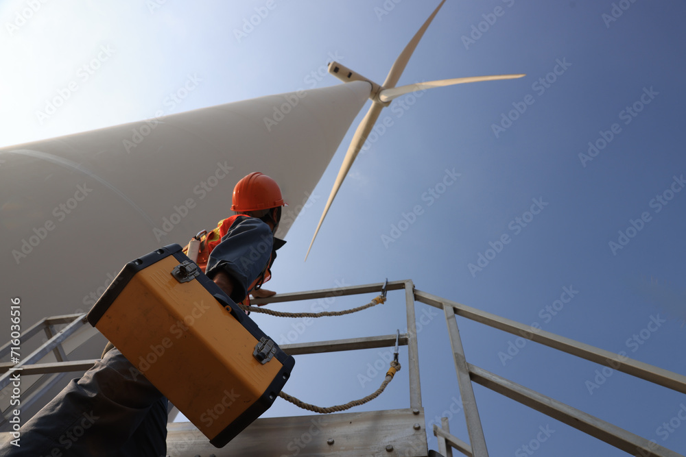 Windmill worker with safety harness and PPE working under wind turbine Windmill worker with safety harness and PPE working under wind turbine
