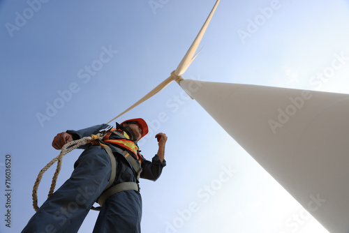 Windmill worker with safety harness and PPE working under wind turbine 