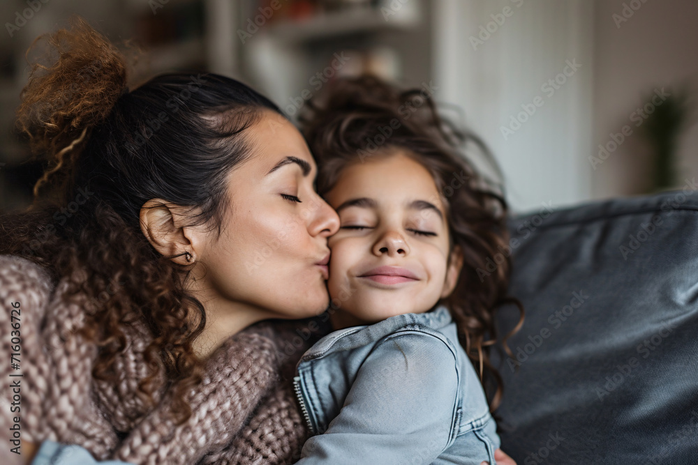 Tender moment of a daughter kissing her mother while sitting together on a sofa at home