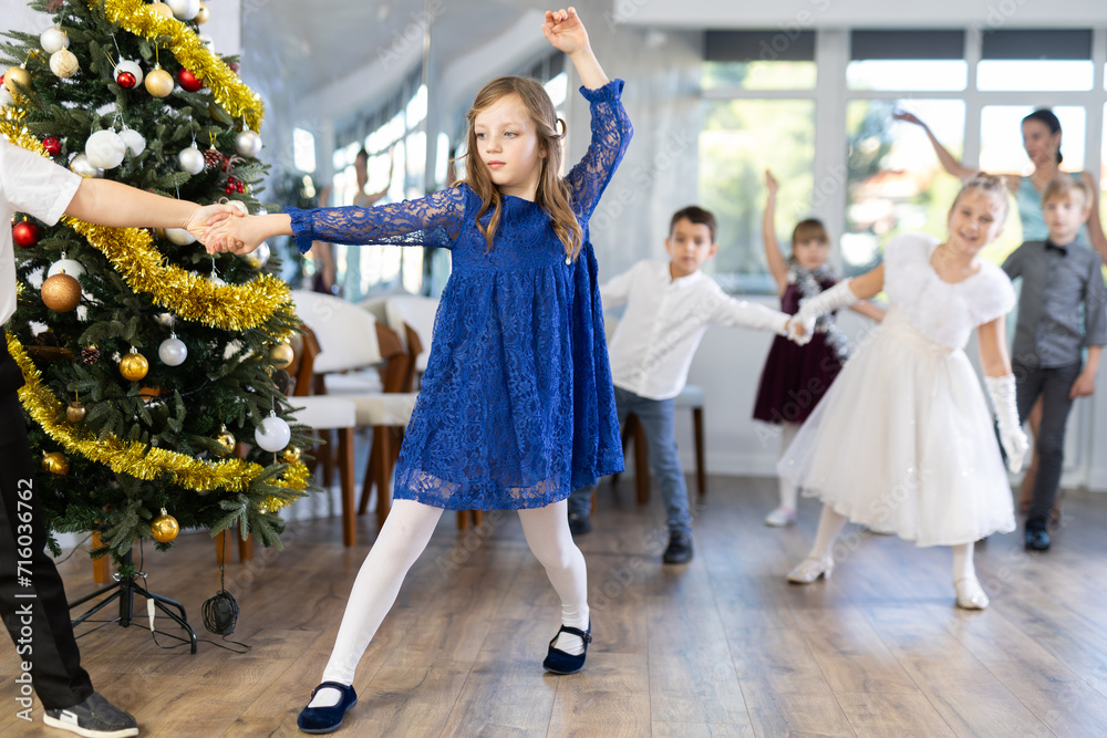 Obraz premium Beautifully dressed little boys and girls dance couple twist dance at Christmas ball near the New Year tree