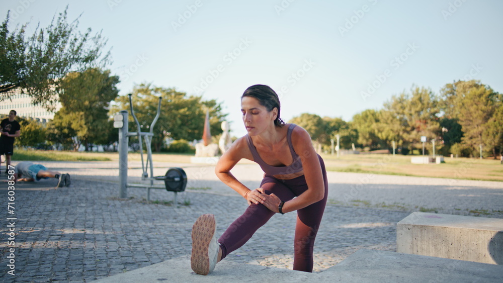 Focused runner warming legs up city stadium. Woman stretching muscles outdoors Focused runner warming legs up city stadium. Woman stretching muscles outdoors