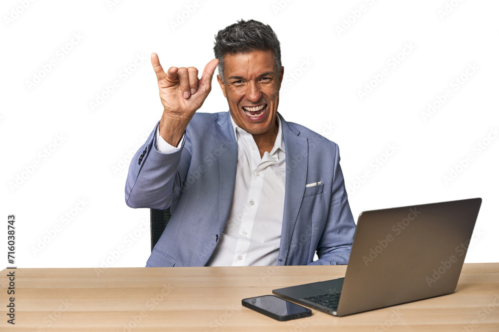 Elegant businessman at desk with laptop showing a horns gesture as a revolution concept. Elegant businessman at desk with laptop showing a horns gesture as a revolution concept.