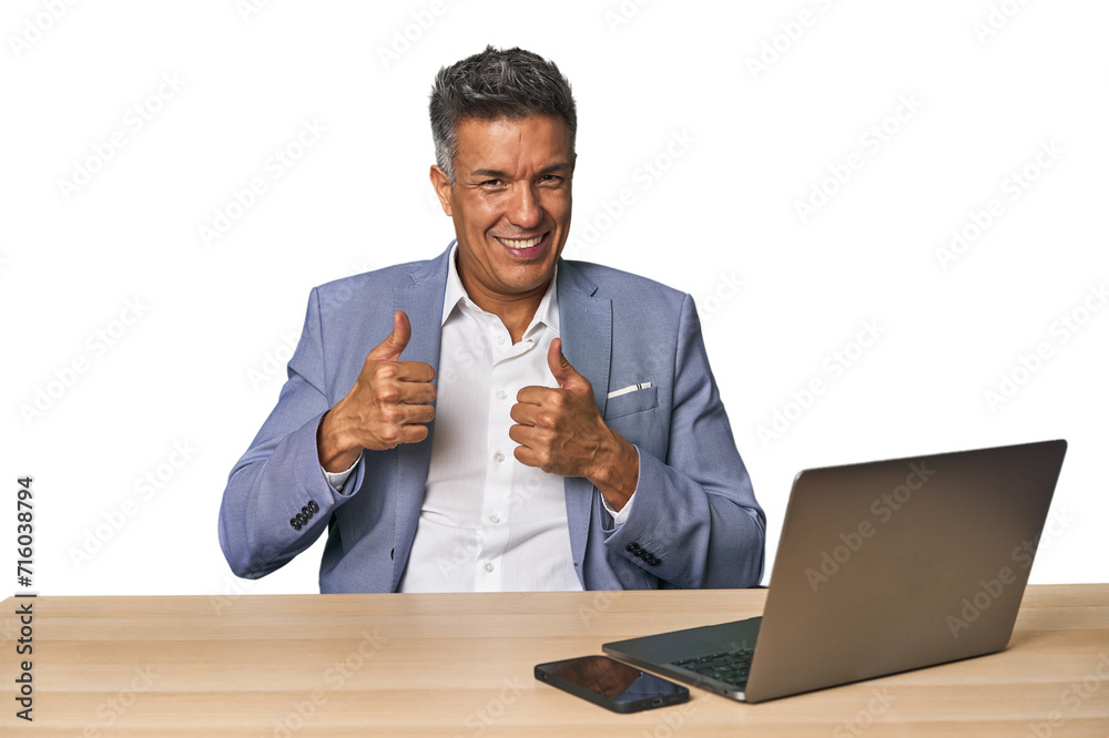 Elegant businessman at desk with laptop raising both thumbs up, smiling and confident.