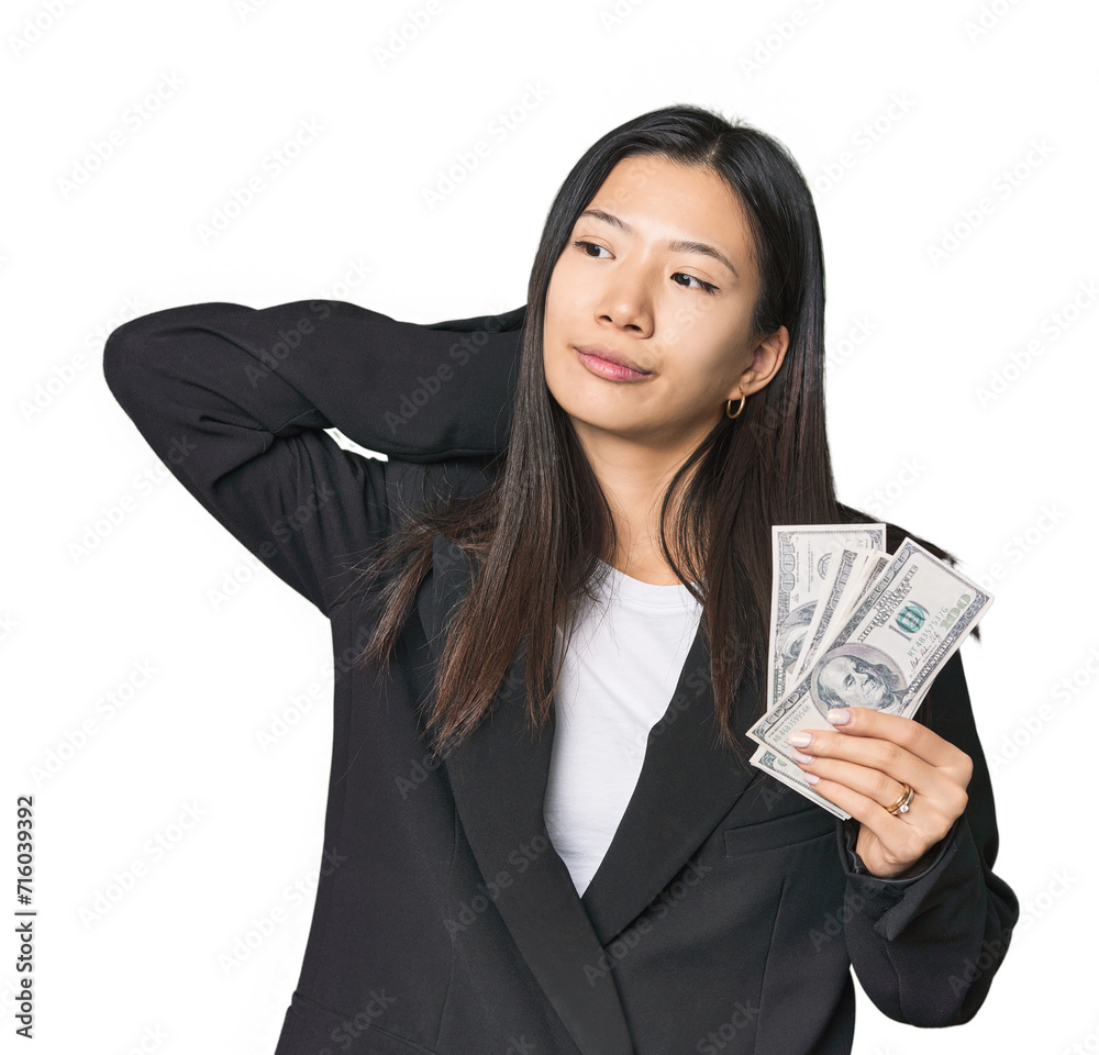 Young Chinese woman with dollars in suit touching back of head, thinking and making a choice. Young Chinese woman with dollars in suit touching back of head, thinking and making a choice.