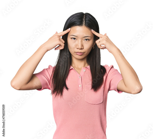 Young Chinese woman in studio setting focused on a task, keeping forefingers pointing head.