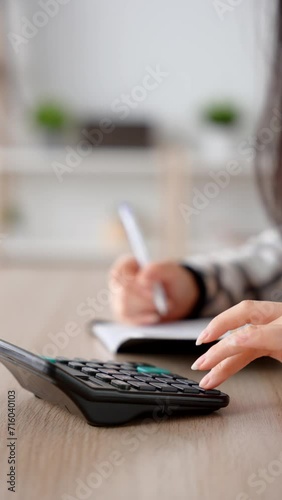 Closeup of hands using calculator and taking notes