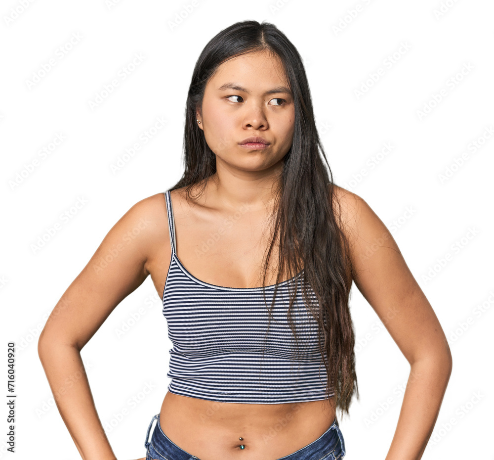 Young Chinese woman in gray top, studio confused, feels doubtful and unsure.