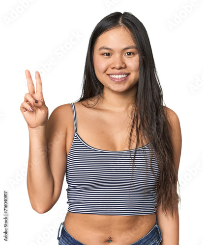 Young Chinese woman in gray top, studio showing victory sign and smiling broadly.