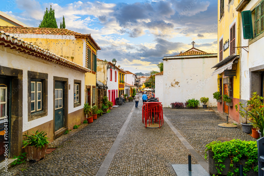Tourists walk down the cobblestone Rua de Santa Maria narrow street of cafes, colorful doors and shops in the historic medieval old town of Funchal, Portugal, on the Canary Island of Madeira. - obrazy, fototapety, plakaty 