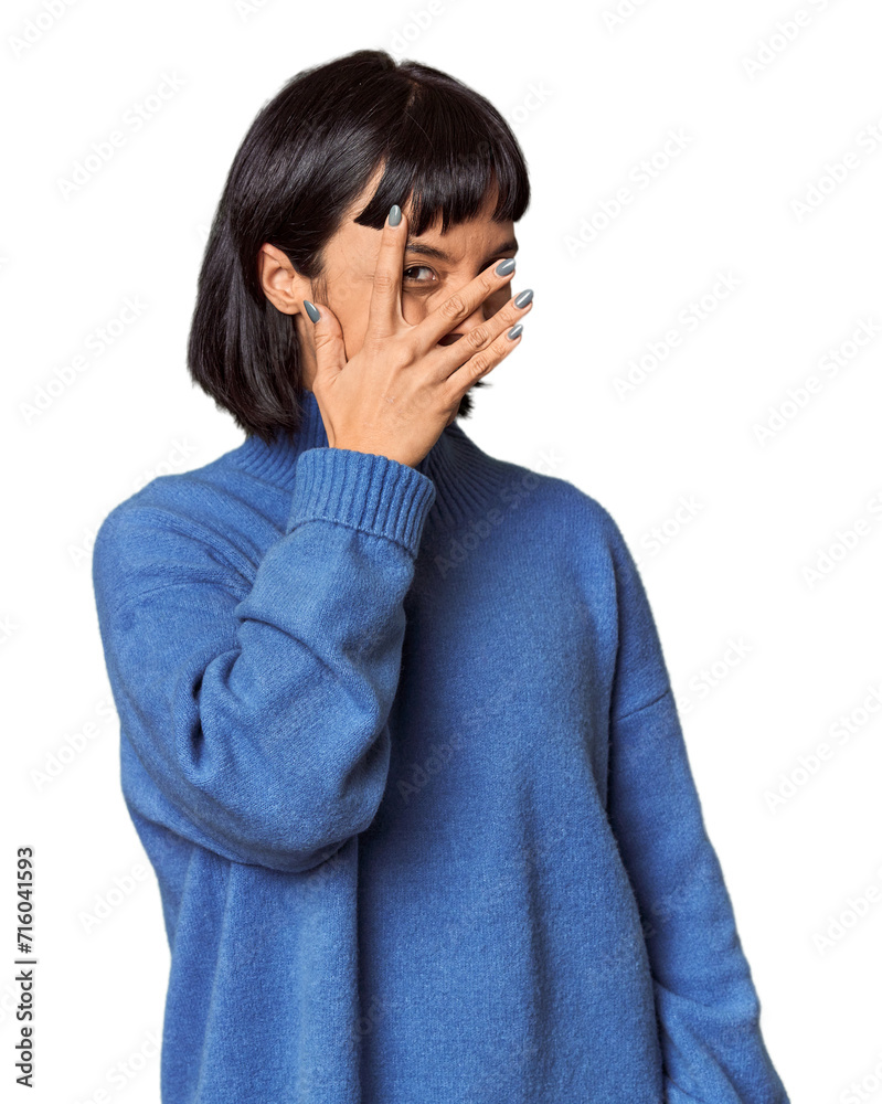 Young Hispanic woman with short black hair in studio blink at the camera through fingers, embarrassed covering face. Young Hispanic woman with short black hair in studio blink at the camera through fingers, embarrassed covering face.