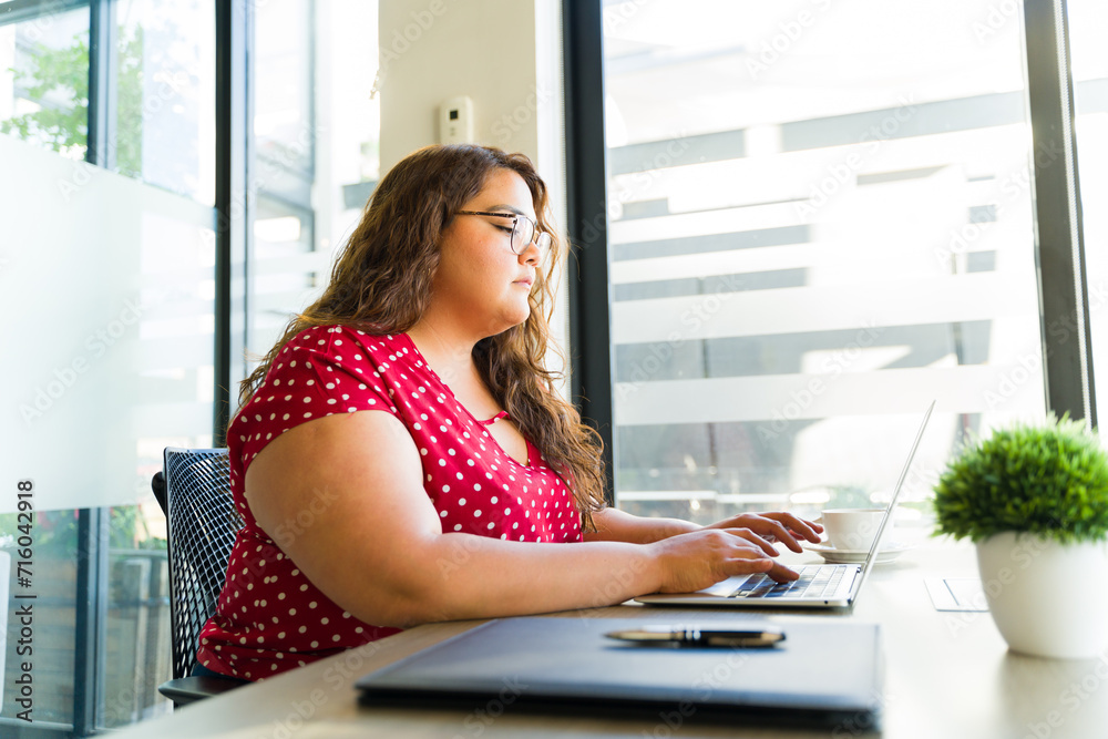 Profile view of a plus size woman using a laptop computer to read her emails in an office Profile view of a plus size woman using a laptop computer to read her emails in an office