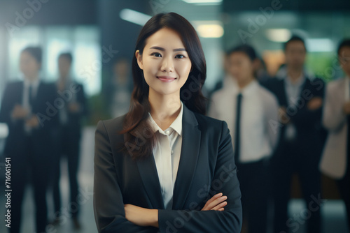 Business woman. Portrait of a asian, beautiful, young and happy woman in a suit standing in a modern office. Smiling female manager looking at the camera in a workplace