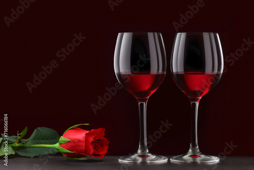 Two glasses of red wine and a rose on a dark background