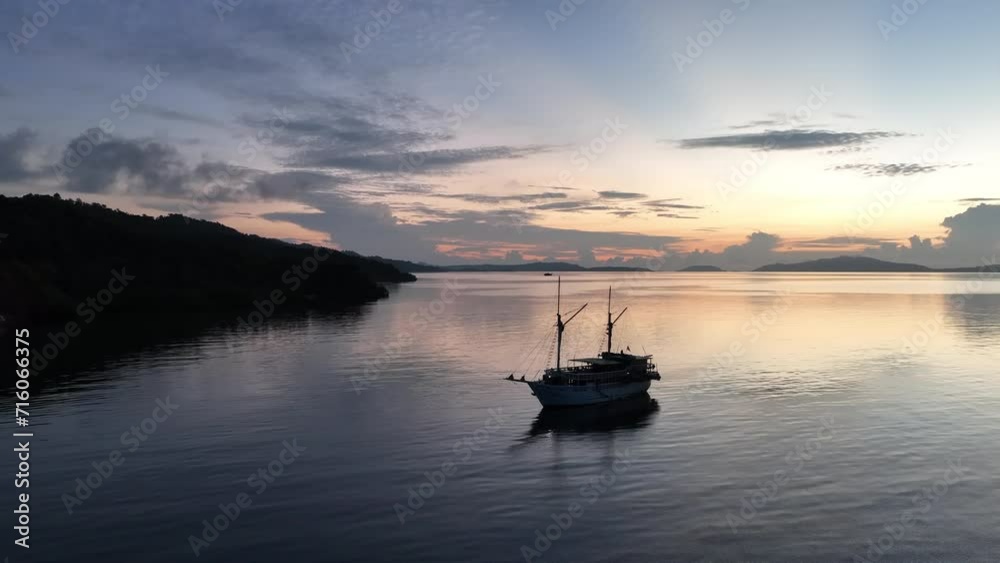 A phinisi schooner, used as a diving liveaboard boat, is silhouetted at sunrise in Raja Ampat, Indonesia. This region is known for its exquisite coral reefs and overall high marine biodiversity. A phinisi schooner, used as a diving liveaboard boat, is silhouetted at sunrise in Raja Ampat, Indonesia. This region is known for its exquisite coral reefs and overall high marine biodiversity.