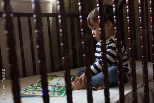 Toddler reading a story book in a crib