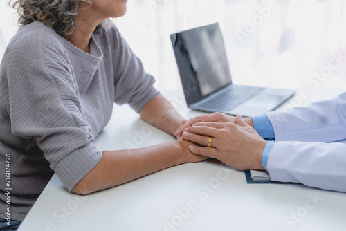 Older female patient and a male doctor with gray hair smiling at each other, hands joined in a comforting gesture.