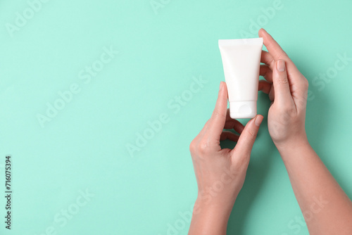 Woman with tube of hand cream on turquoise background, top view. Space for text