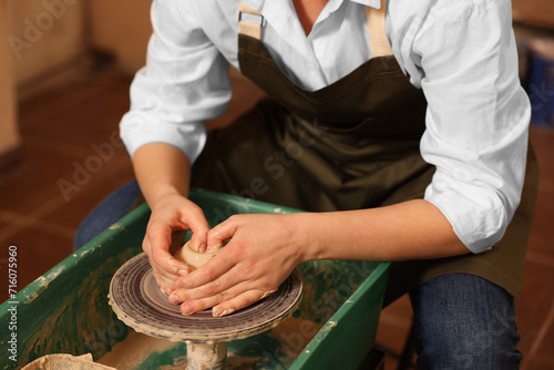 Woman crafting with clay on potter's wheel indoors, closeup