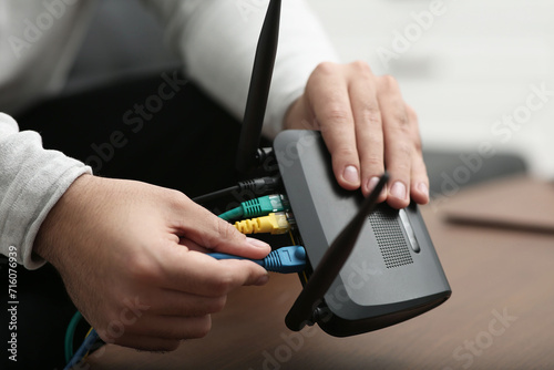 Man inserting cable into Wi-Fi router at wooden table indoors, closeup