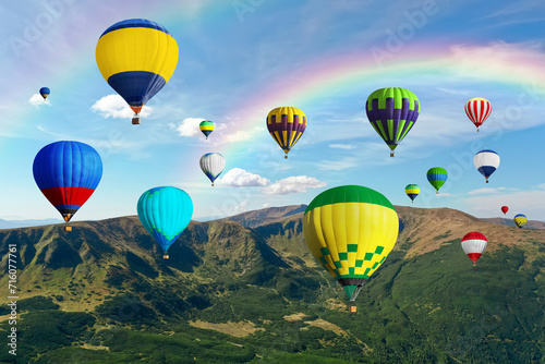 Bright hot air balloons flying in sky with rainbow over mountain © New Africa