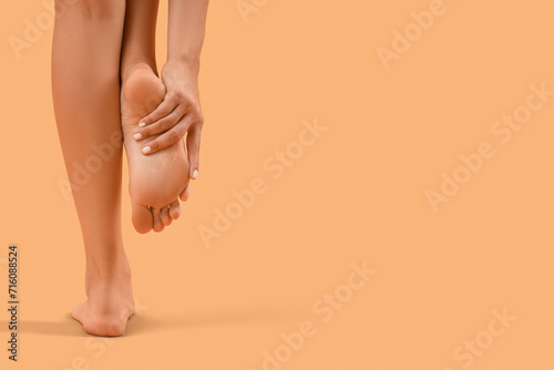 Beautiful young woman making foot massage on orange background, back view