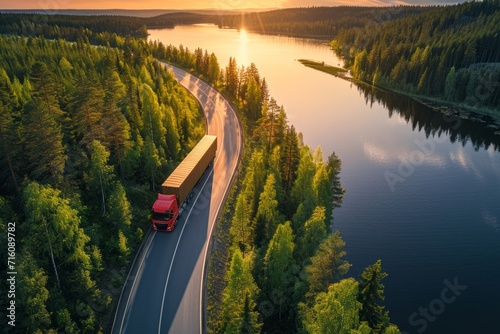 Beautiful sunset landscape in Karelia Russia with truck and trailer on a curved road by a lake surrounded by green pine forest photo