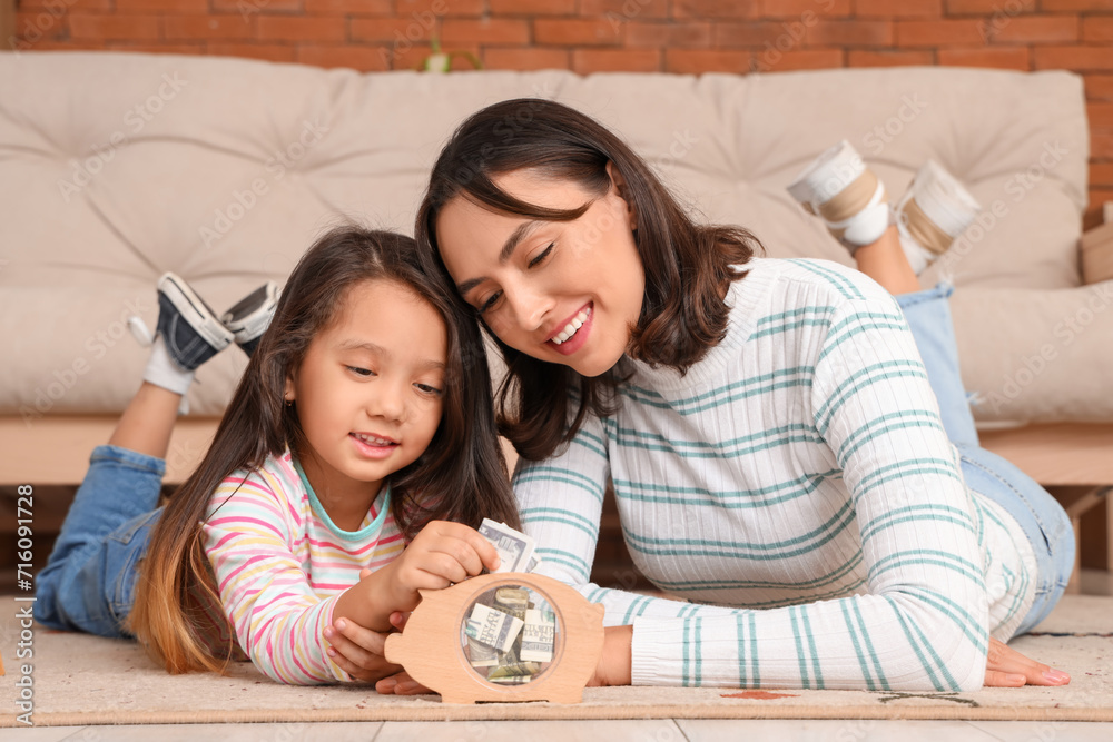 Little girl with her mother putting money into piggy bank at home Little girl with her mother putting money into piggy bank at home