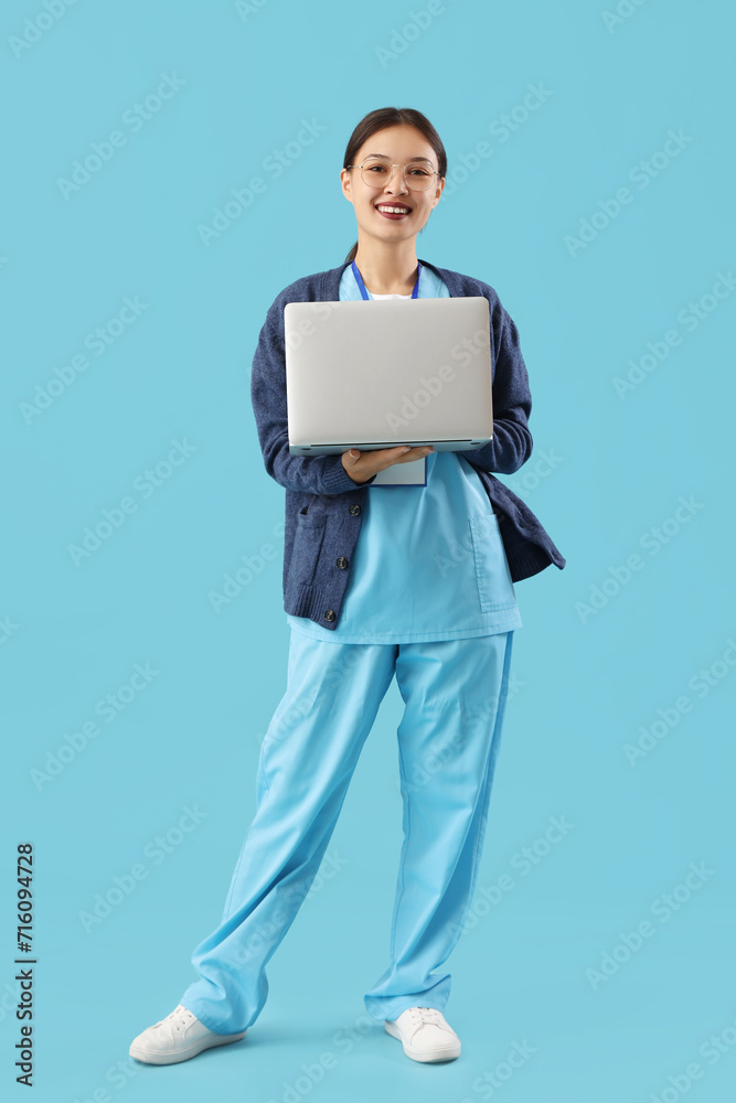 Asian medical intern with laptop on blue background Asian medical intern with laptop on blue background