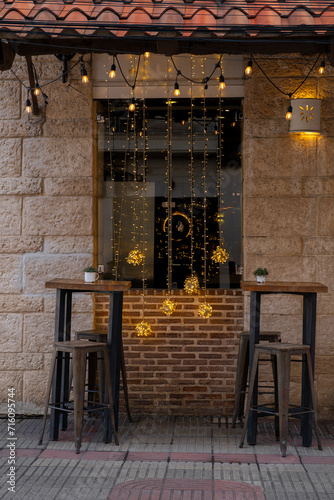 Two empty small tables and chairs in front of the window with light decorations of a small cozy cafe. Shot at pedestrian El Conde street in Santo Domingo historical center, Dominican Republic.
