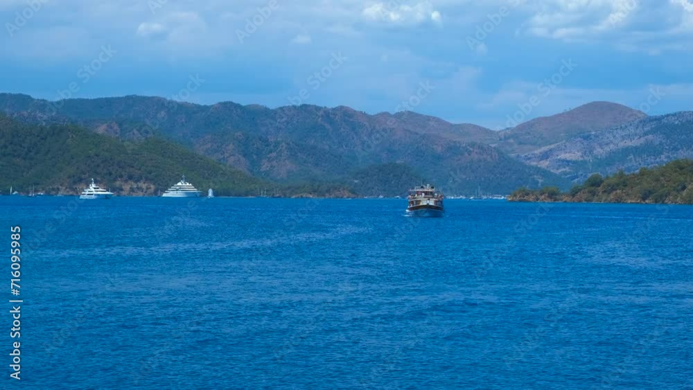 Sailing ship across bay water by mountains. A view of big wooden ship transporting the tourists across the tropical bay against sunny sky in summer. Sailing ship across bay water by mountains. A view of big wooden ship transporting the tourists across the tropical bay against sunny sky in summer.