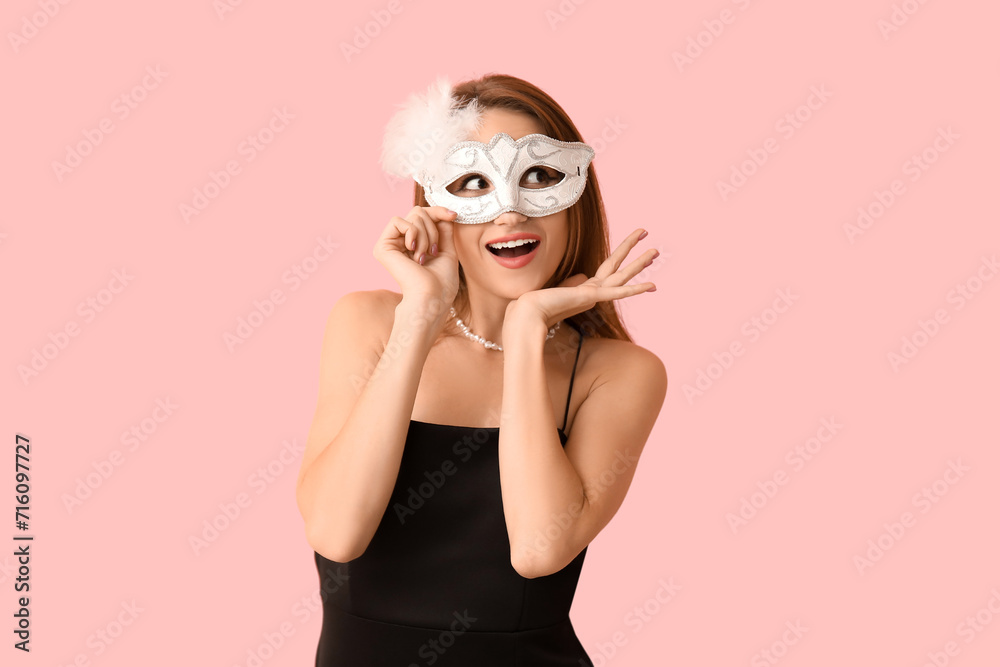 Happy young woman in white carnival mask on pink background Happy young woman in white carnival mask on pink background