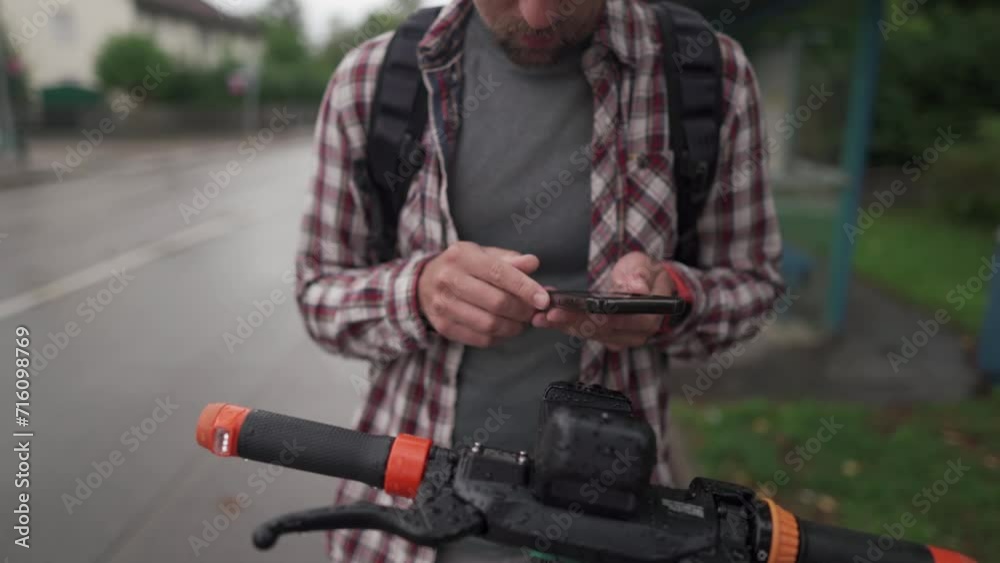 Man uses smartphone to rent an electric scooter in city. Young guy paying for e-scooter via online payment using his mobile phone. Theme of electric vehicle rental. Urban eco-friendly transport. Man uses smartphone to rent an electric scooter in city. Young guy paying for e-scooter via online payment using his mobile phone. Theme of electric vehicle rental. Urban eco-friendly transport.