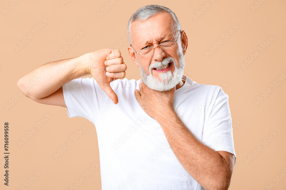 Ill old man with sore throat showing thumb-down on beige background Ill old man with sore throat showing thumb-down on beige background