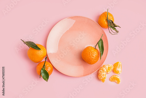 Plate with tasty tangerines and leaves on pink background