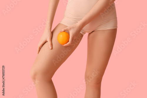 Beautiful young woman with cellulite problem and orange on pink background