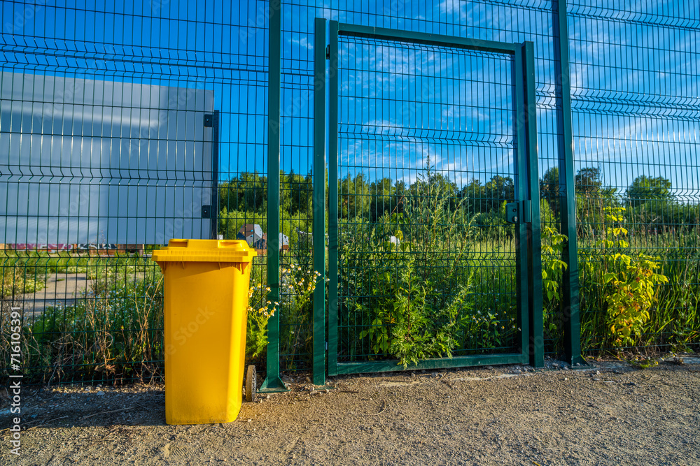 A yellow garbage container in the park in summer. A yellow garbage container in the park in summer.