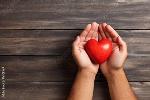 Top view of a young man holding a red heart on a light wooden background  with room for text. Depicting the idea of donation.