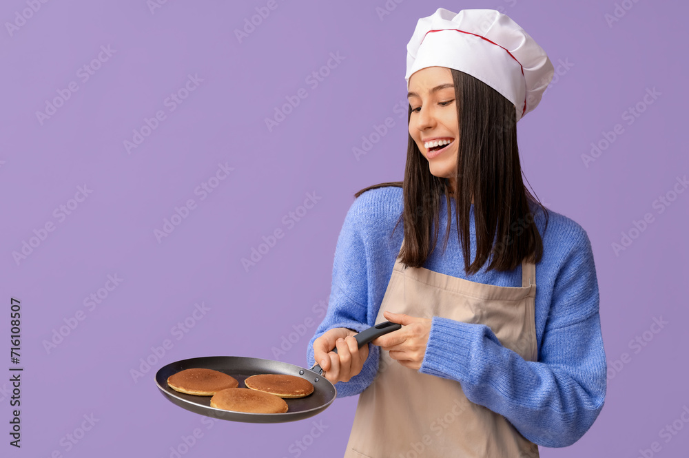 Young female chef holding frying pan with tasty pancakes on lilac background Young female chef holding frying pan with tasty pancakes on lilac background