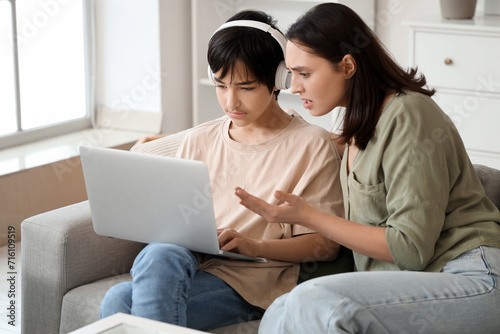 Teenage boy in headphones with laptop ignoring his mother at home. Family problem concept