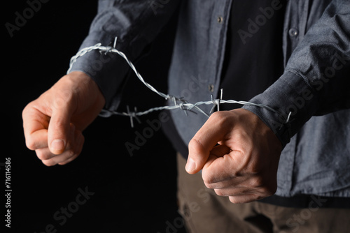 Young Jewish man with barbed wire on black background, closeup. International Holocaust Remembrance Day