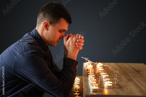 Young Jewish man with burning candles praying on black background. International Holocaust Remembrance Day photo