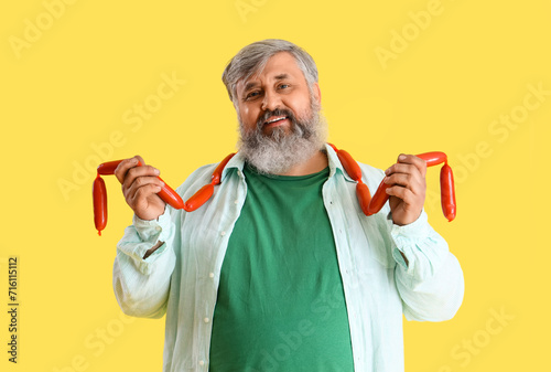 Mature man with tasty sausages on yellow background