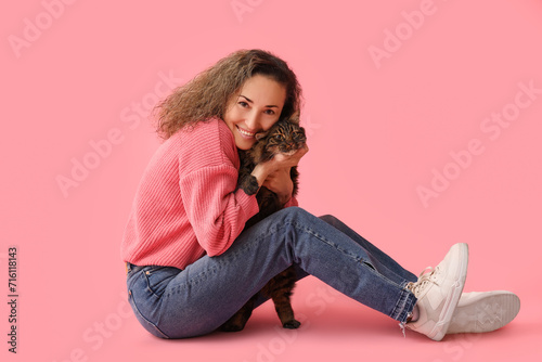 Happy mature woman with cute cat sitting on pink background