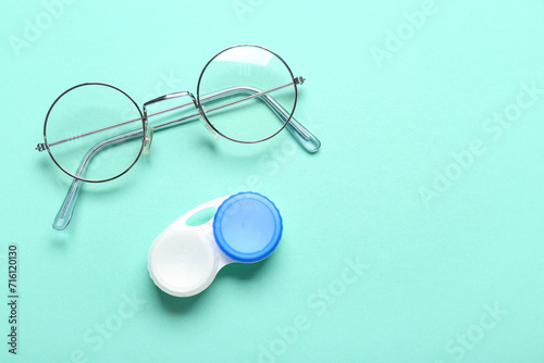 Eyeglasses and container for contact lenses on turquoise background