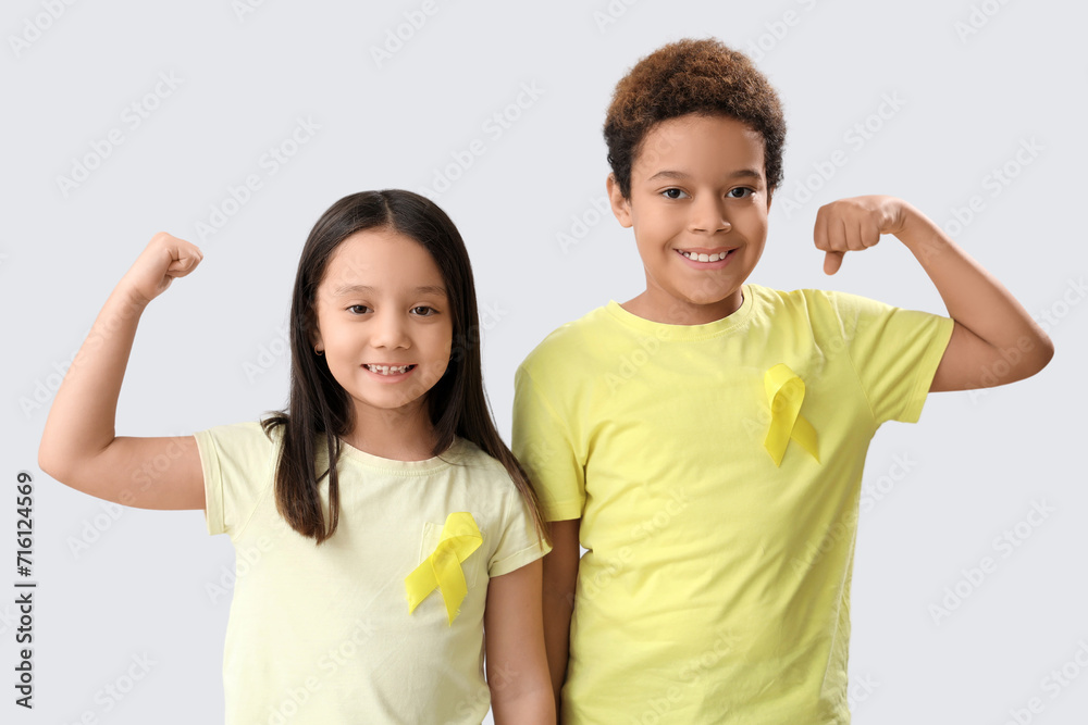 Cute little children with yellow ribbons showing muscles on grey background. Childhood cancer awareness concept Cute little children with yellow ribbons showing muscles on grey background. Childhood cancer awareness concept