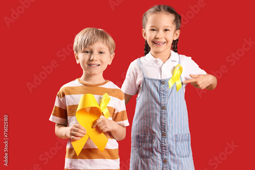 Cute little children with yellow ribbons on red background. Childhood cancer awareness concept