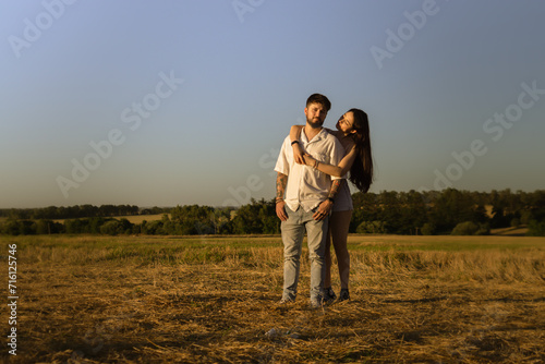 Beautiful couple hugging and kissing in a field at sunset