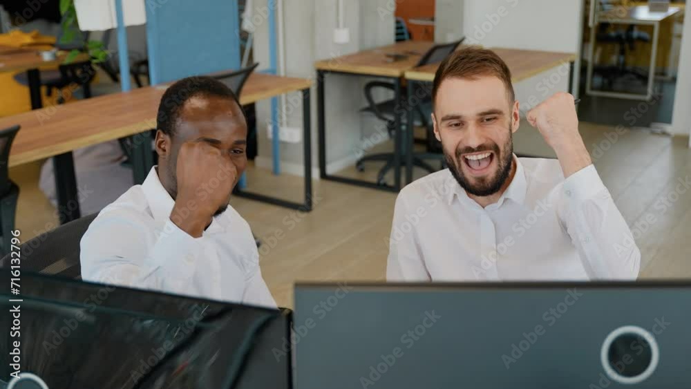 Two diverse traders sitting at desk at office together monitoring stocks data candle charts on screen Two diverse traders sitting at desk at office together monitoring stocks data candle charts on screen